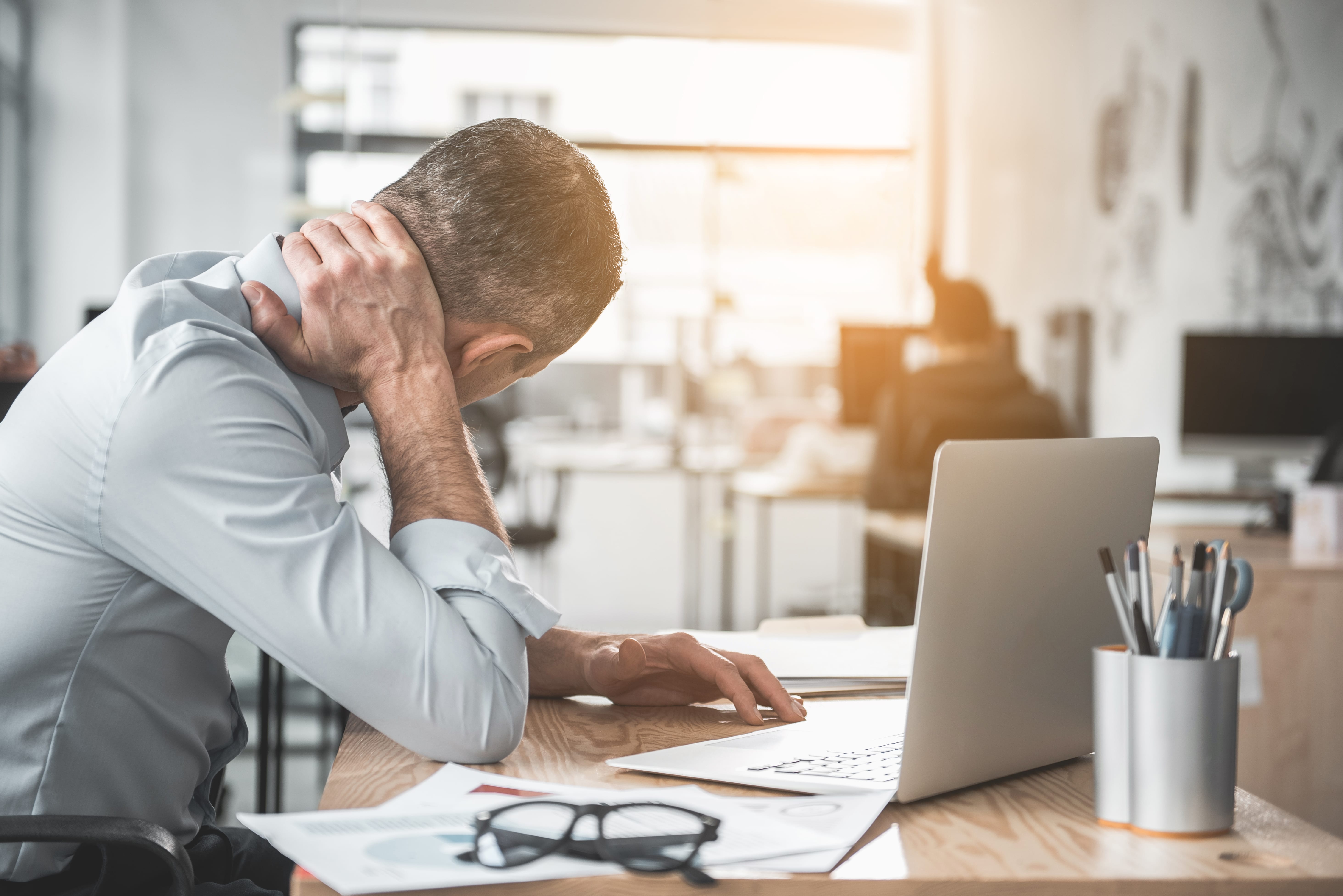 Photo d'une personne assis devant son bureau et qui se maintient le cou à cause de douleurs